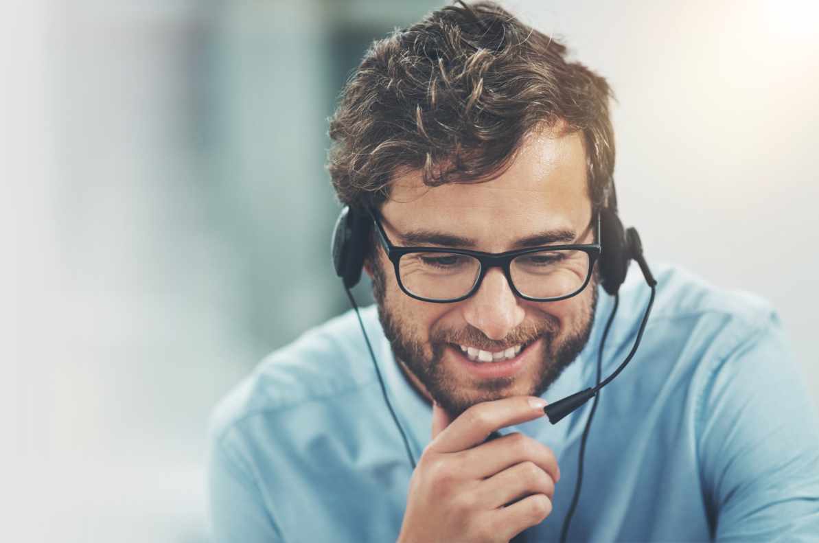 Customer service man with blue shirt and headset leaning forward with chin in hands and smiling